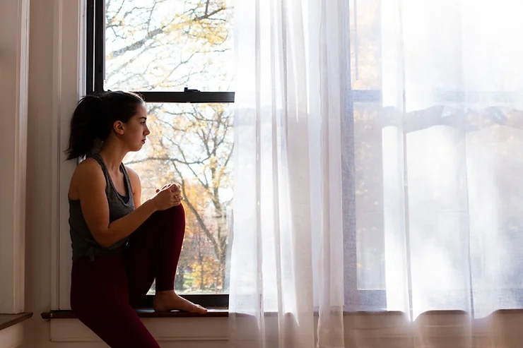 Pencere kenarında oturan kişinin doğal gün ışığı alan iç mekandaki deneyimini gösteren fotoğraf